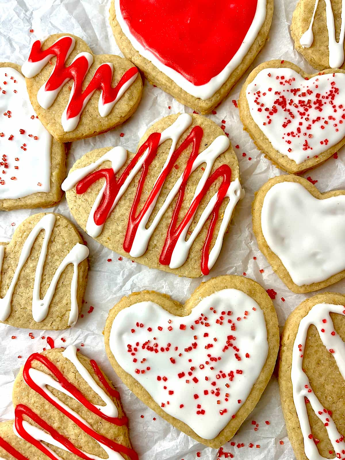 Numerous heart-shaped cookies decorated for Valentine's Day with red and white icing.