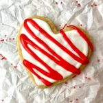 A heart-shaped vegan sugar cookie with red and white icing.