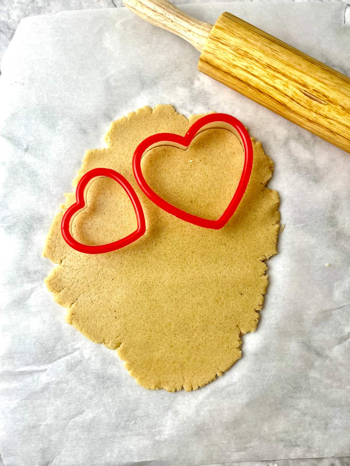 Rolled out cookie dough with two heart-shaped cookie cutters on the dough.