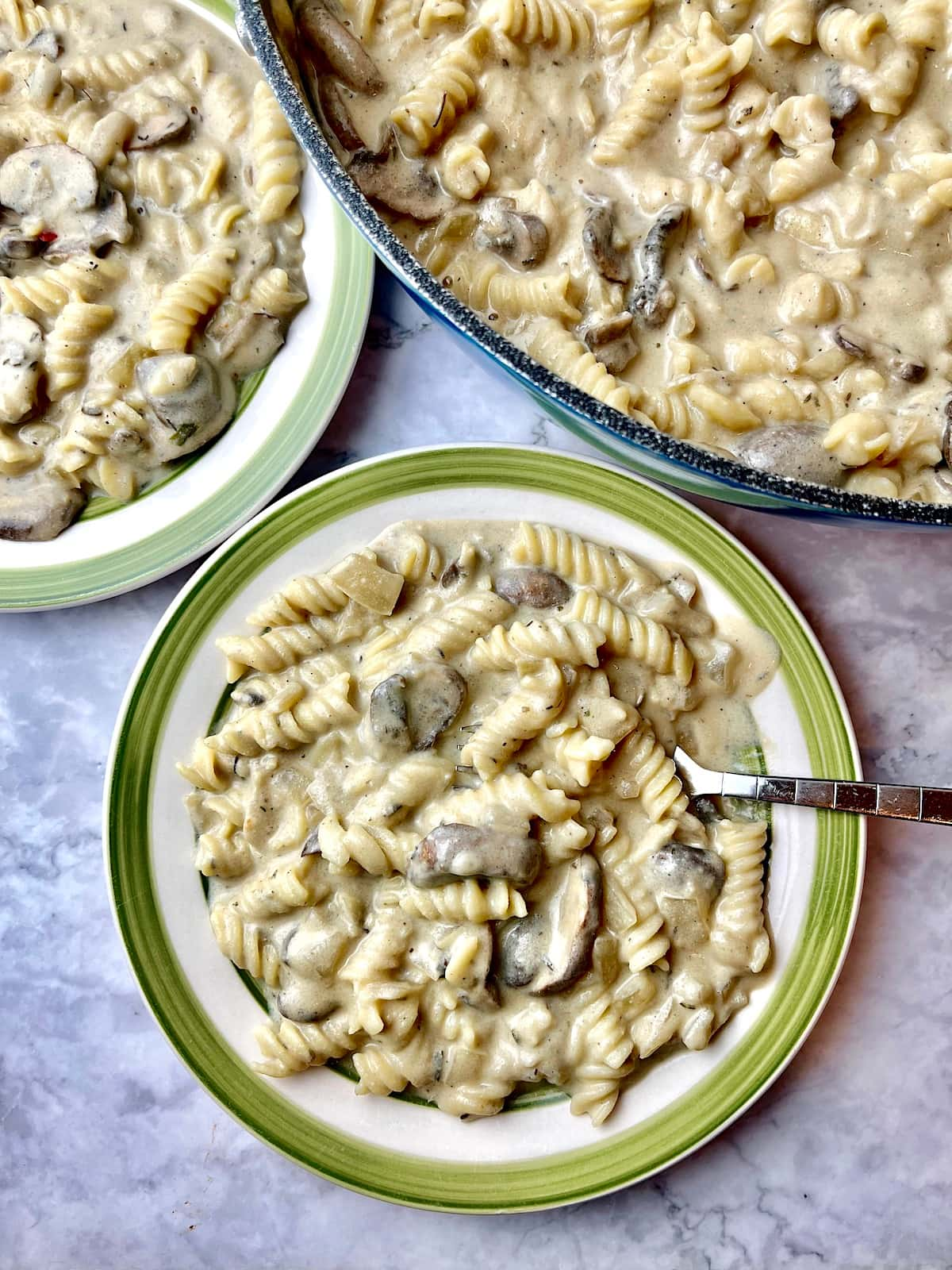 Two plates of vegan mushroom stroganoff next to a large pan of mushroom stroganoff.