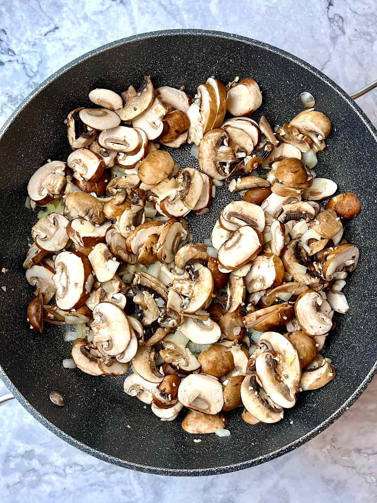 A large pan of sliced mushrooms and chopped onion.