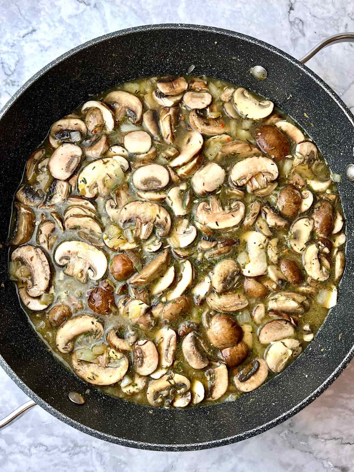 A large pan of mushrooms, onion, and vegetable broth.