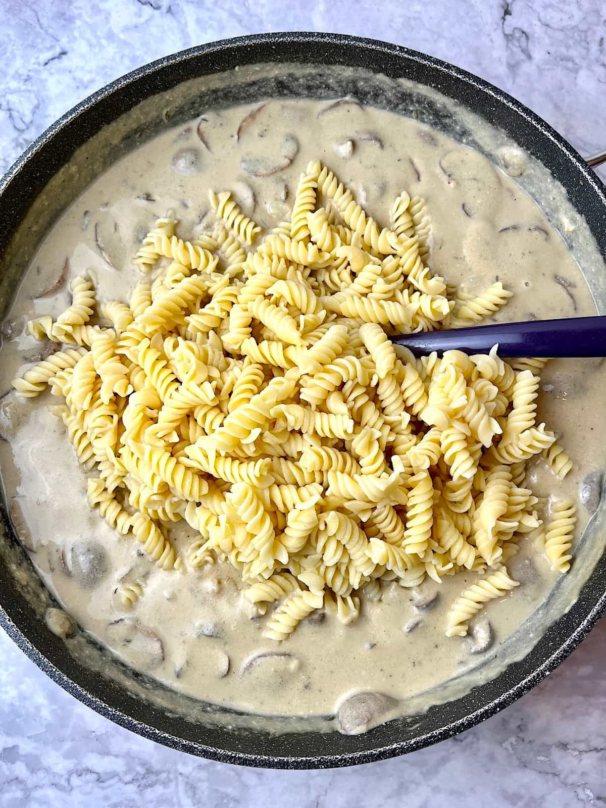 A pan of vegan mushroom stroganoff with fusilli pasta poured on top.