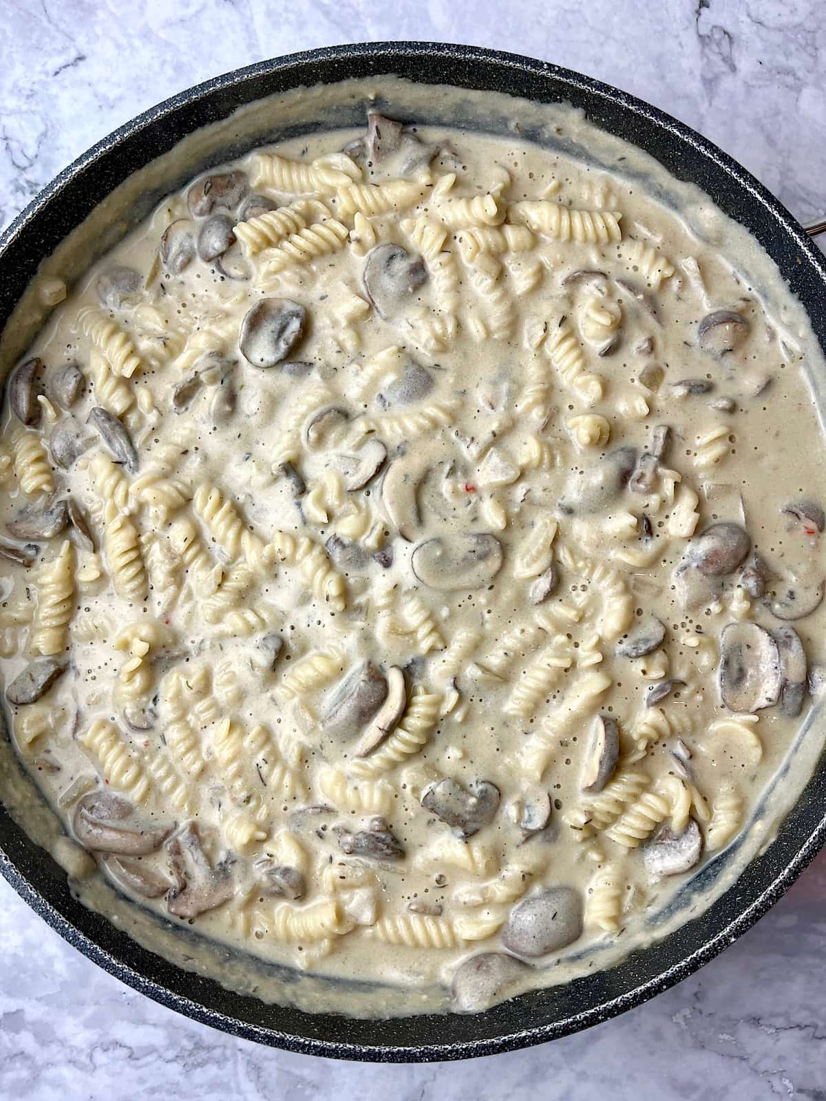 A large pan of vegan mushroom stroganoff mixed with fusilli pasta.