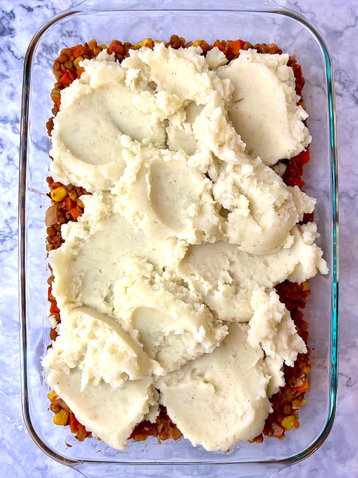 A large dish with mashed potatoes on top of a lentil shepherd's pie filling.