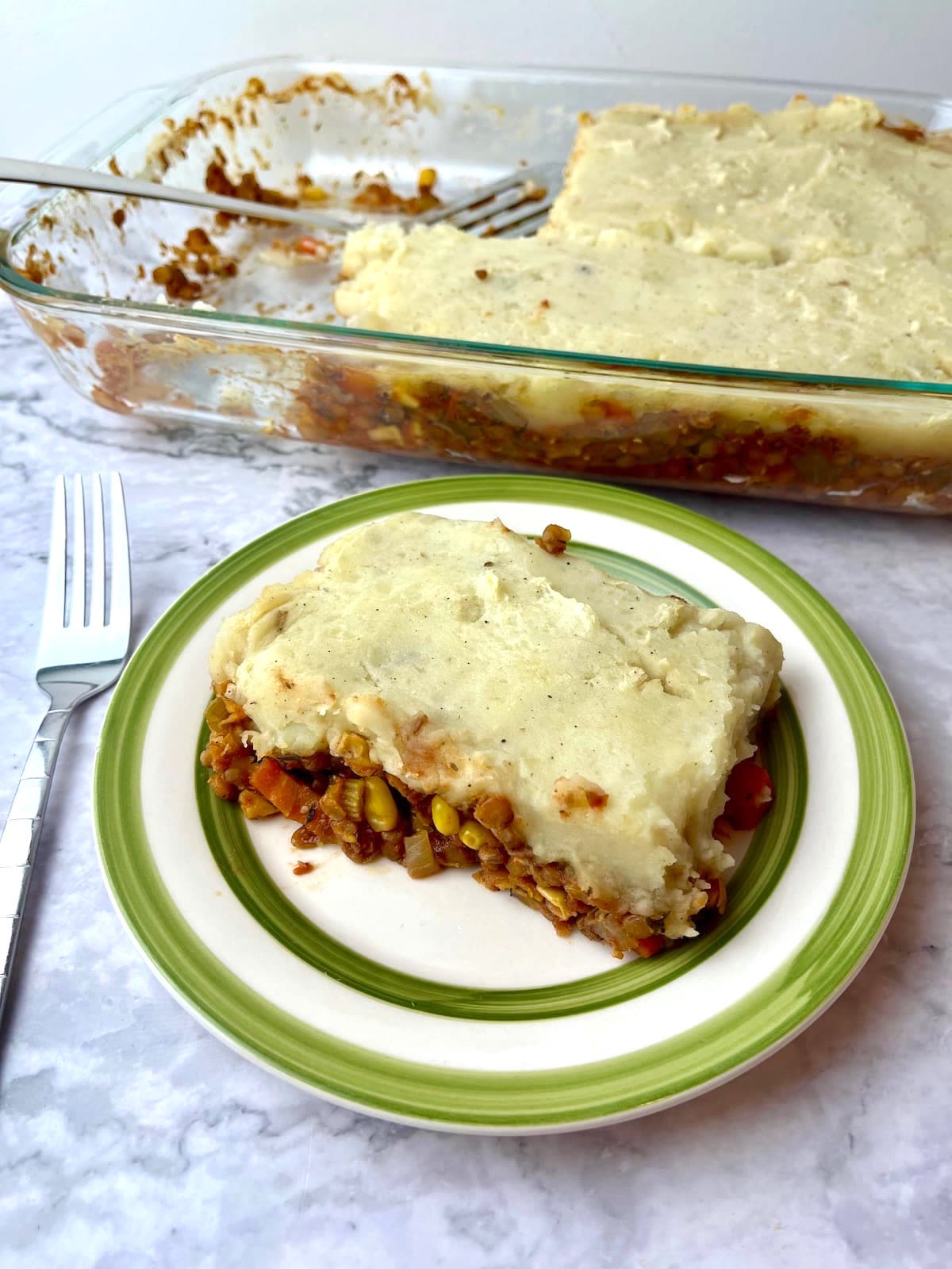 A baking dish of lentil shepherd's pie next to a piece of it on a plate.