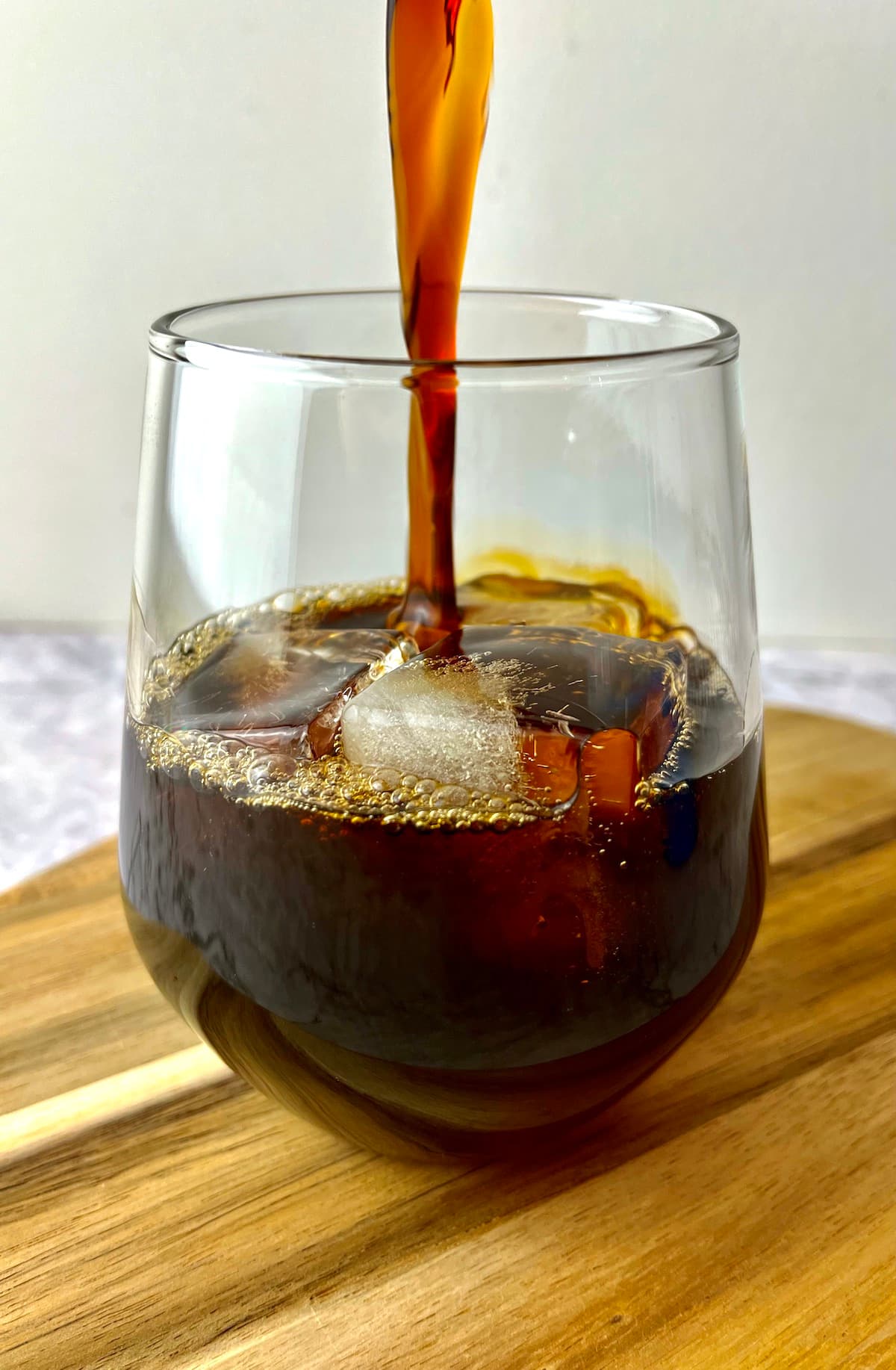 Coffee being poured over ice into a glass on a wooden board.