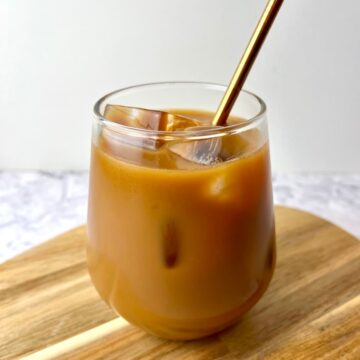 A glass of vegan iced coffee on a wooden cutting board.