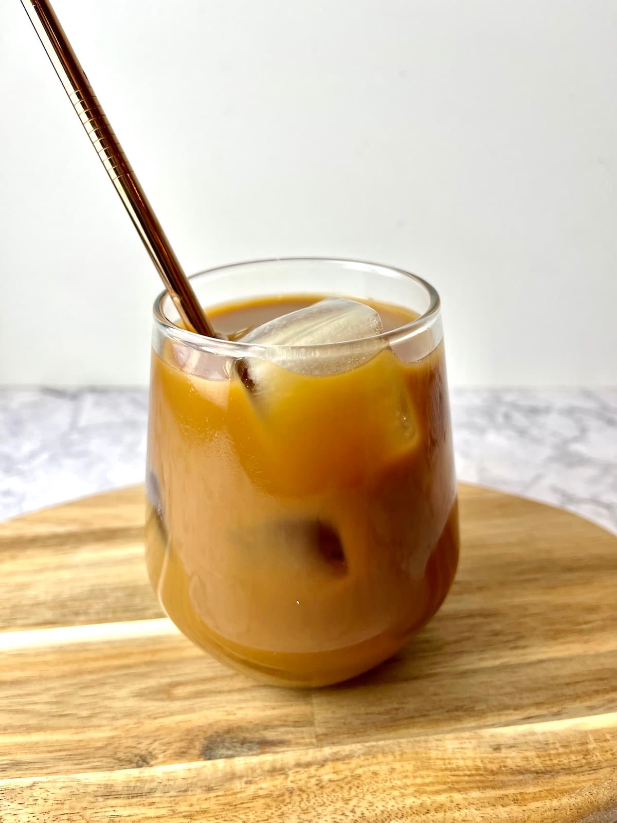 A glass of vegan iced coffee on a wooden cutting board.