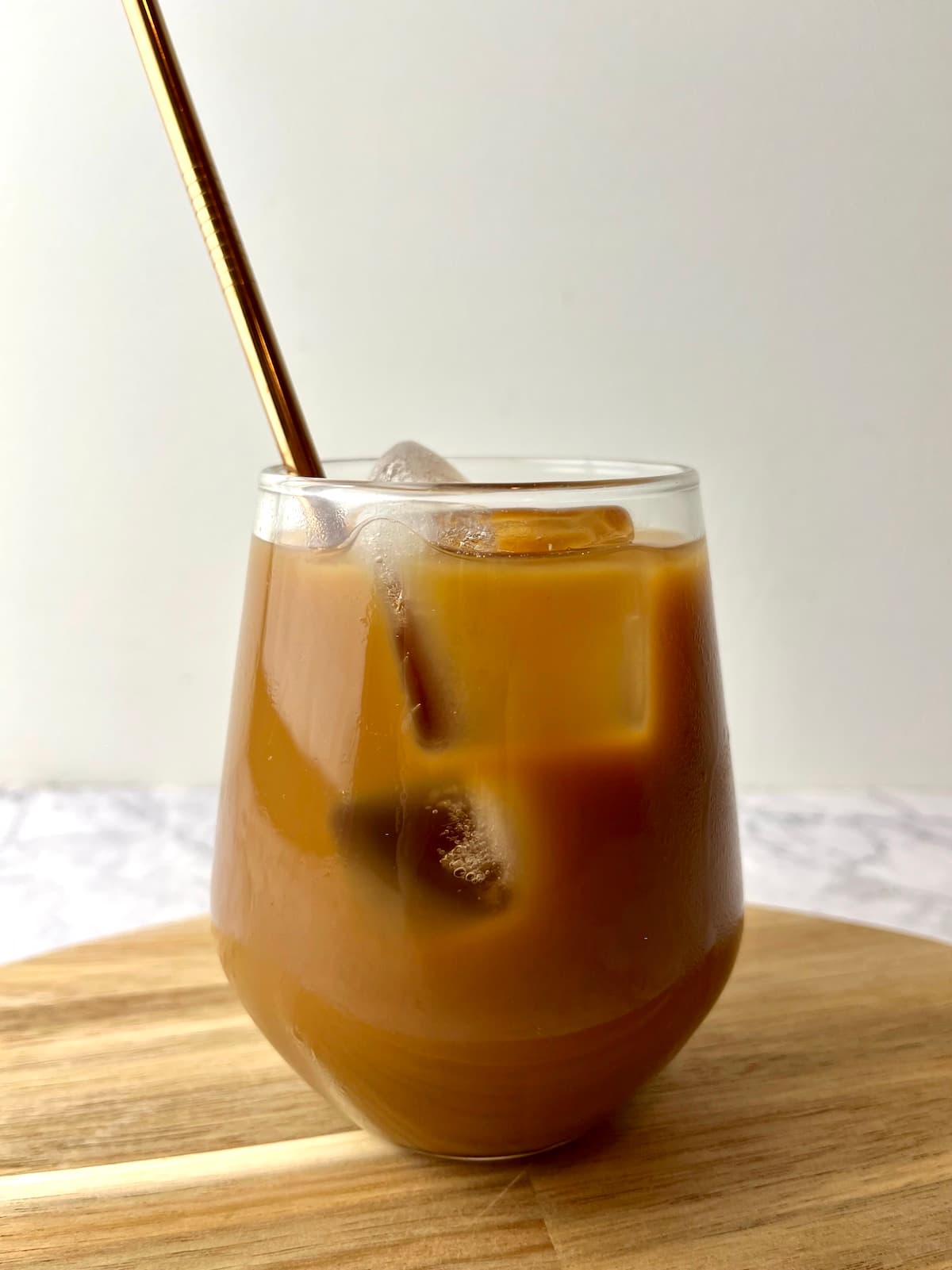 A glass of oat milk iced coffee on a wooden cutting board.