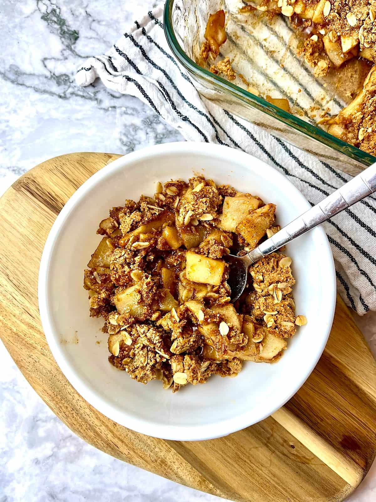 A bowl of peanut butter apple crisp sitting on a wooden cutting board.