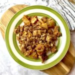 A plate of peanut butter apple crisp sitting on a wooden cutting board.