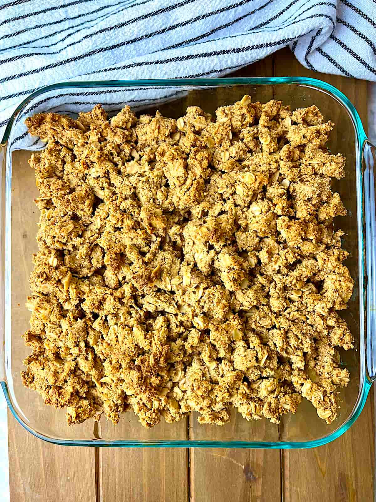 Baked peanut butter apple crisp in a square baking dish on a wooden board.