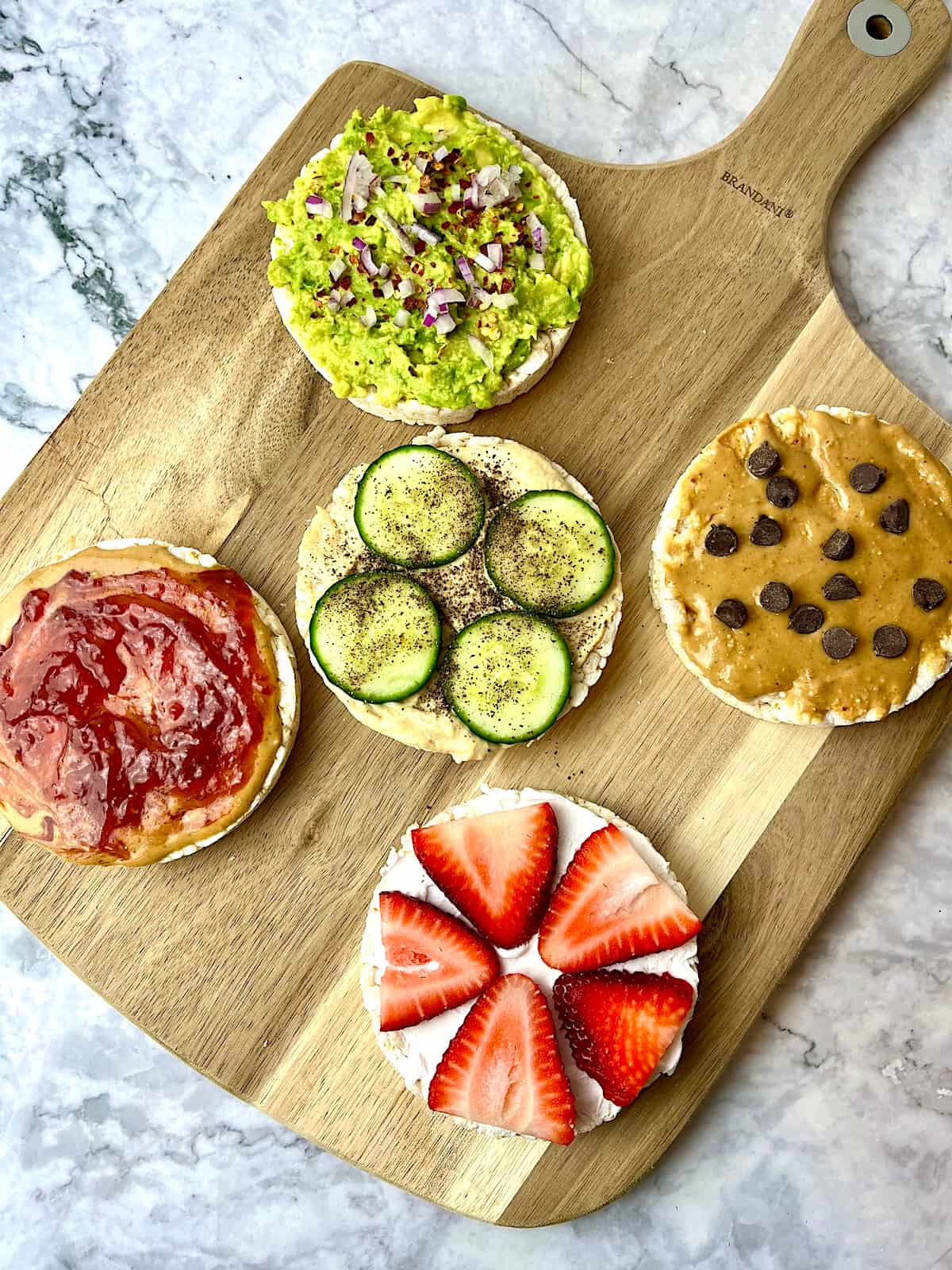 Five rice cakes on a cutting board, all topped with various vegan toppings.