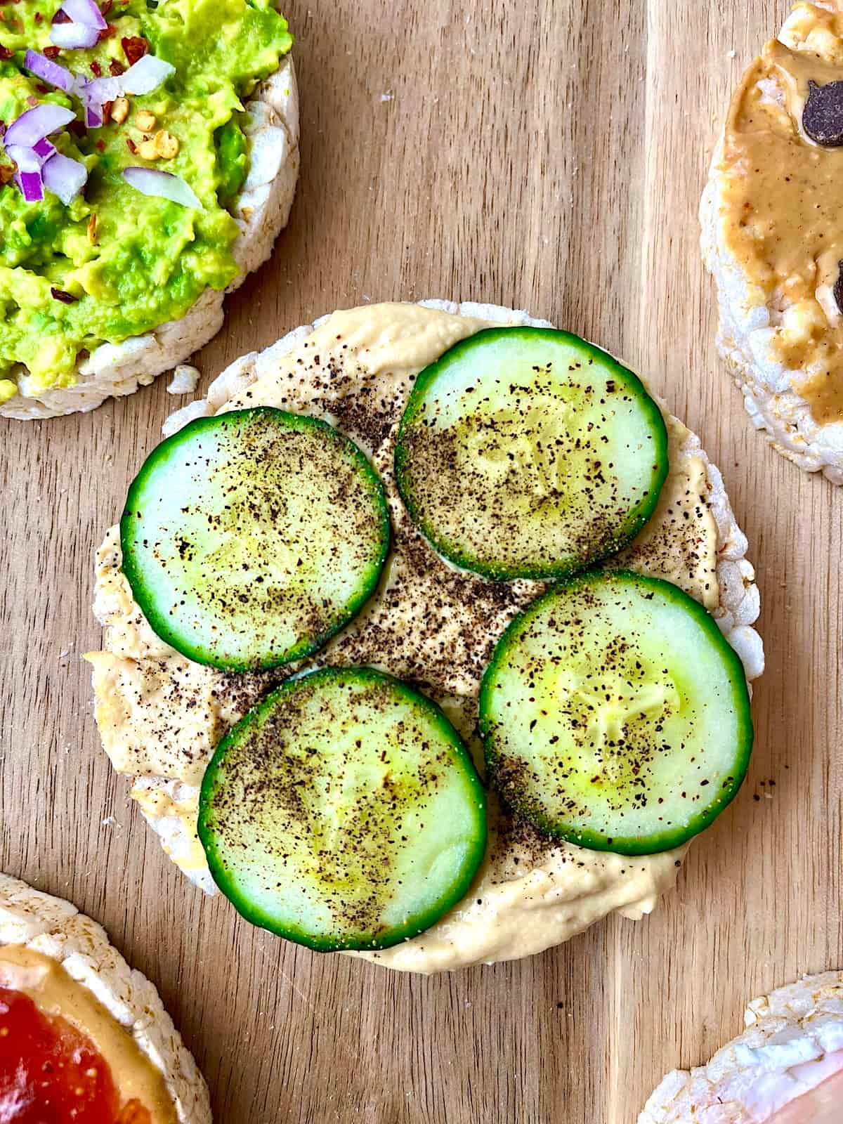 A rice cake topped with hummus, cucumber slices, and pepper.