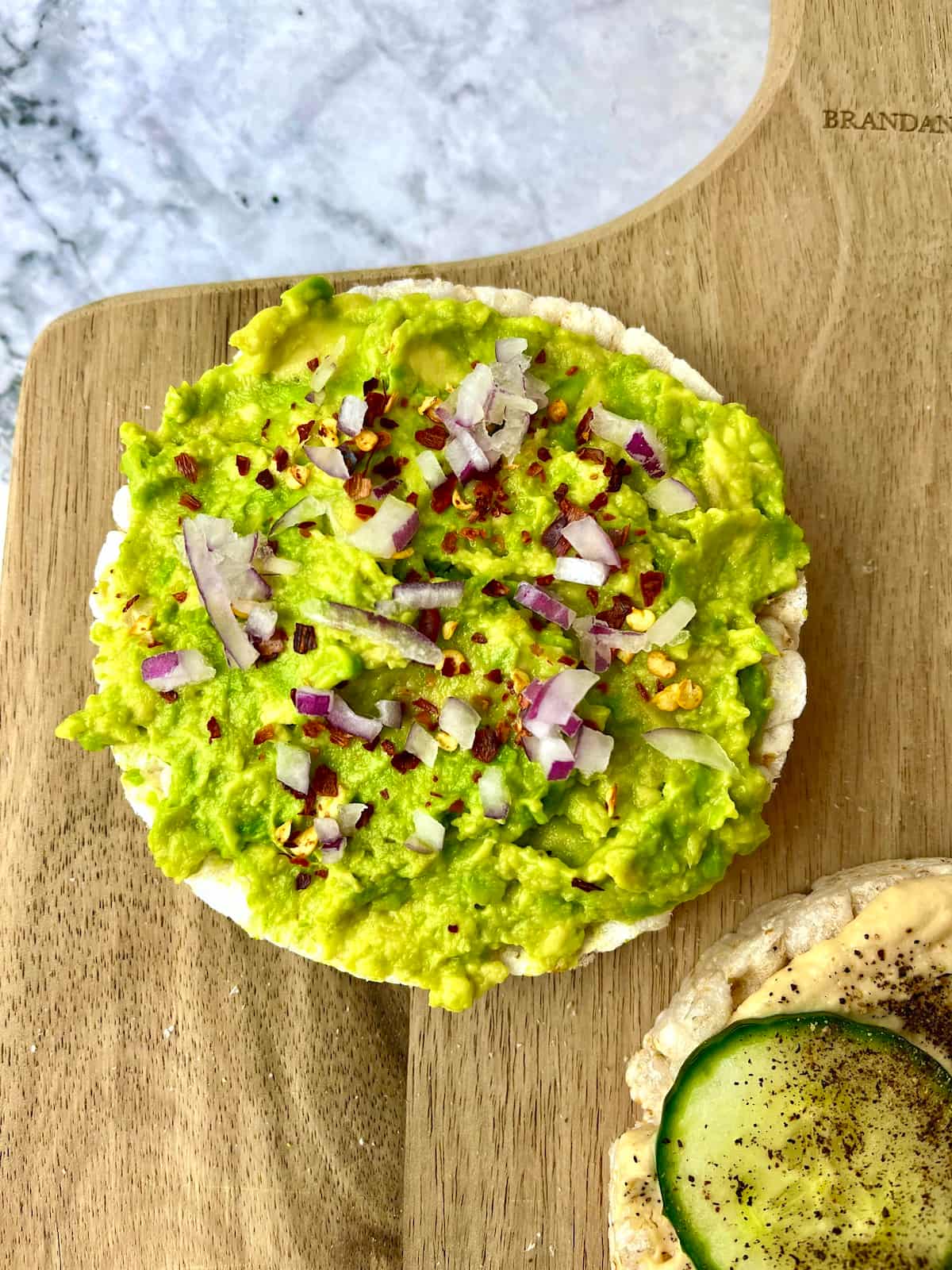 A rice cake topped with mashed avocado, red onion, and crushed red pepper.