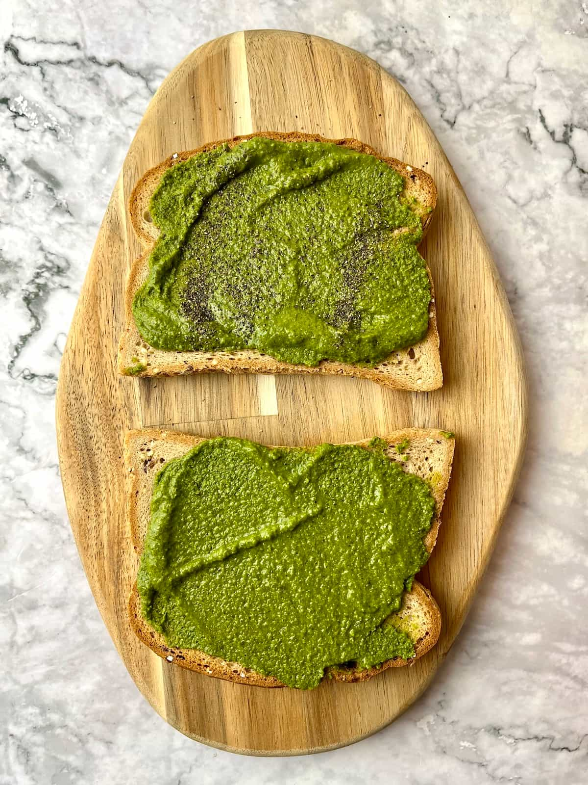 Two slices of bread, both with pesto spread on them.