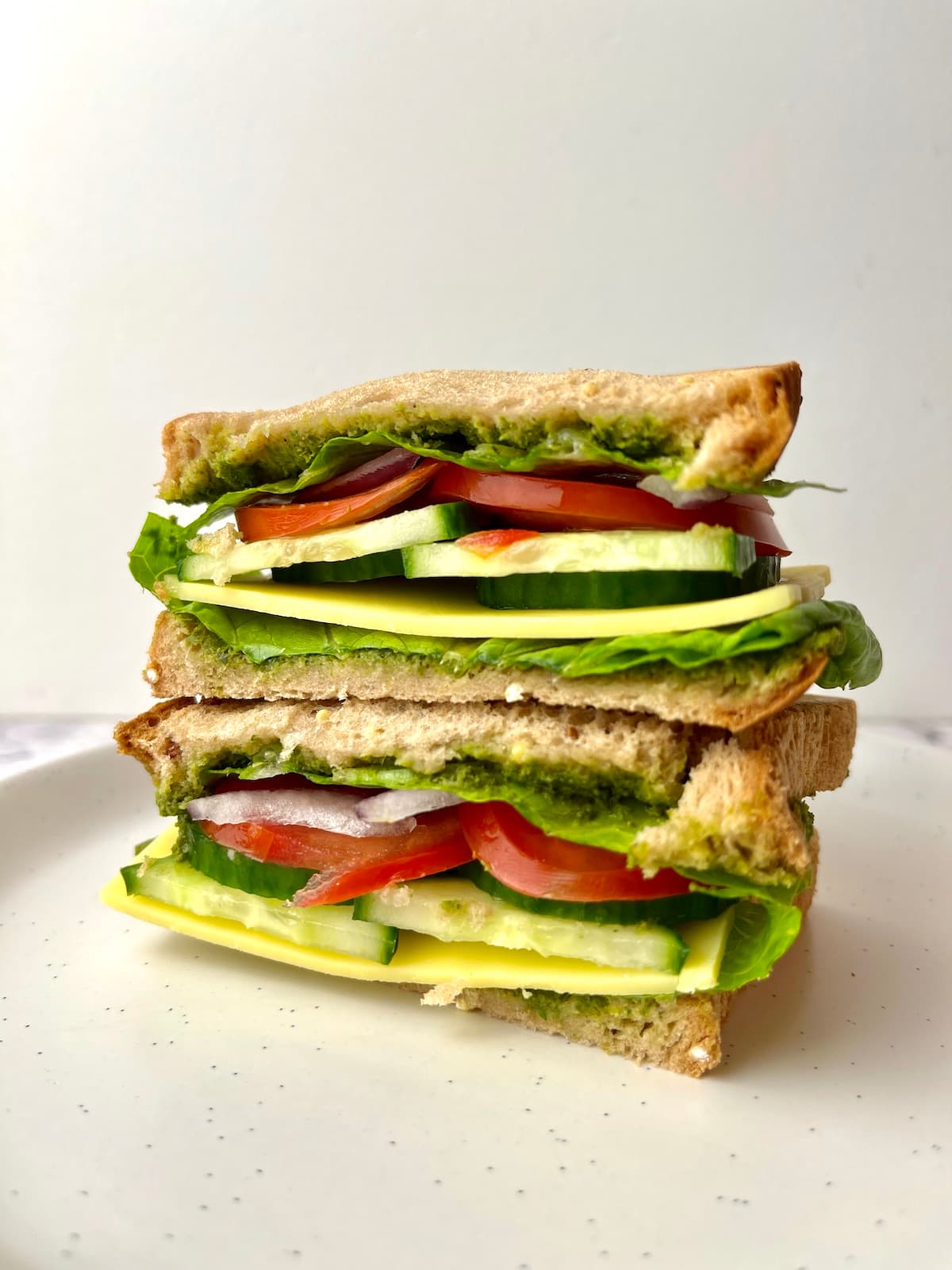 Two veggie pesto sandwich halves stacked on top of each other.