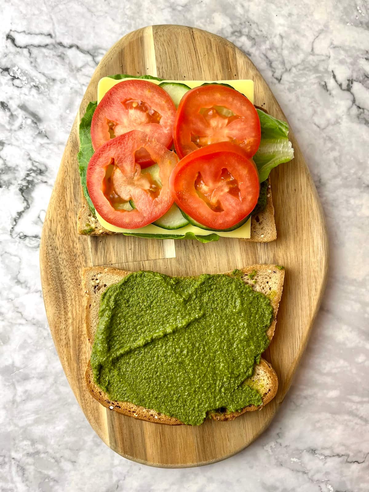 Two slices of bread, one with pesto, and the other with veggies with tomato slices on top.