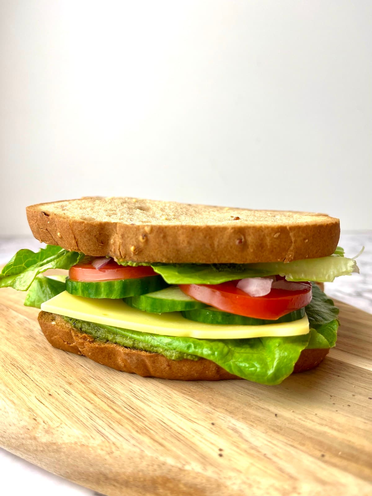 A veggies pesto sandwich on a wooden cutting board.