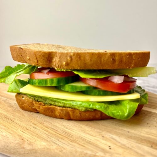 A veggies pesto sandwich on a wooden cutting board.