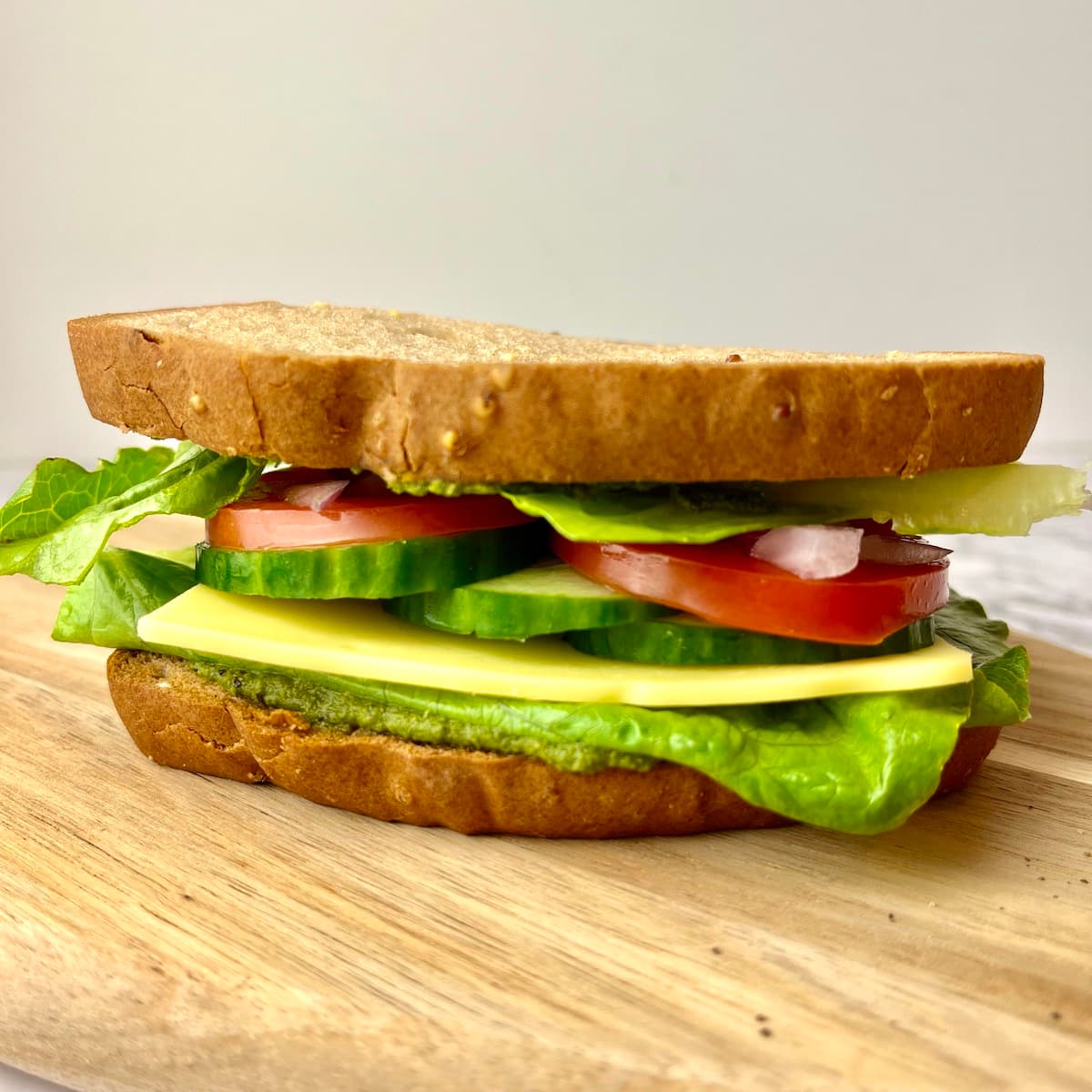 A veggies pesto sandwich on a wooden cutting board.