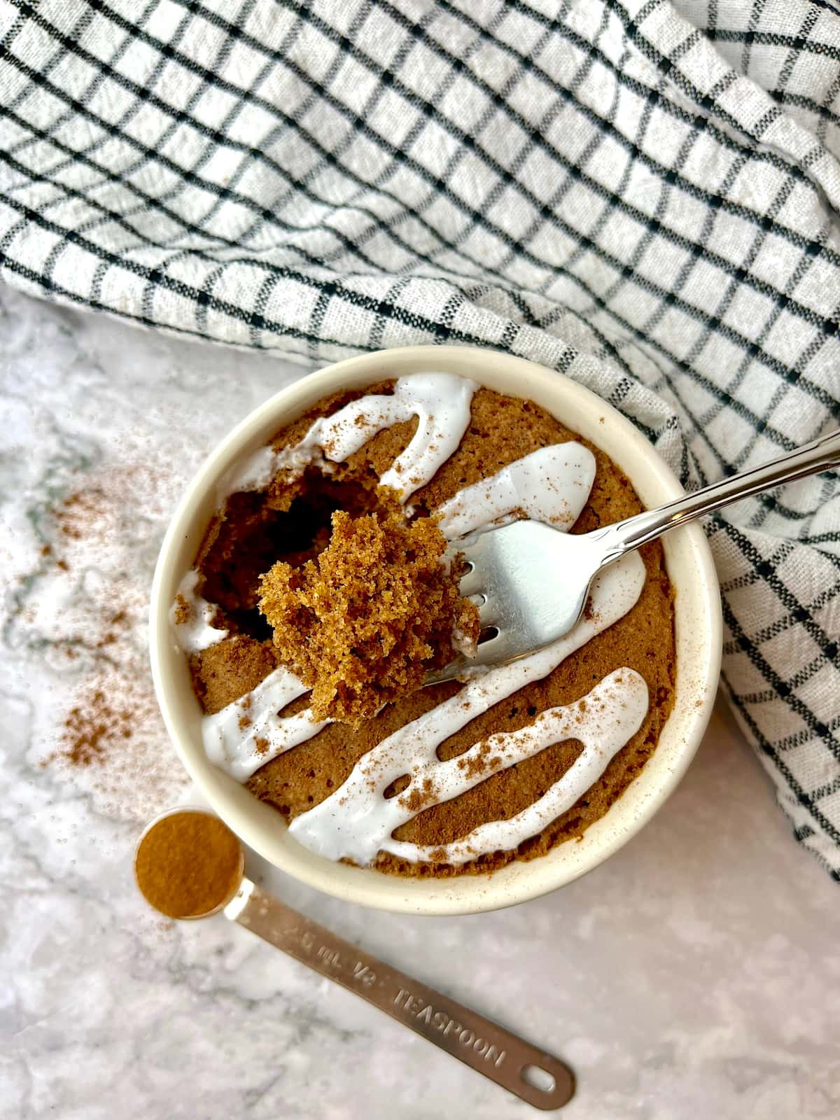 A forkful of cake on top of a cinnamon mug cake with white icing.