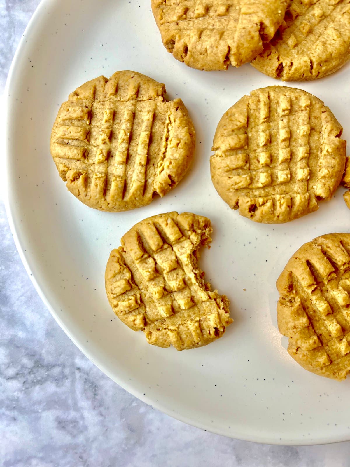 Peanut butter cookies on a plate, one with a bite taken out of it.