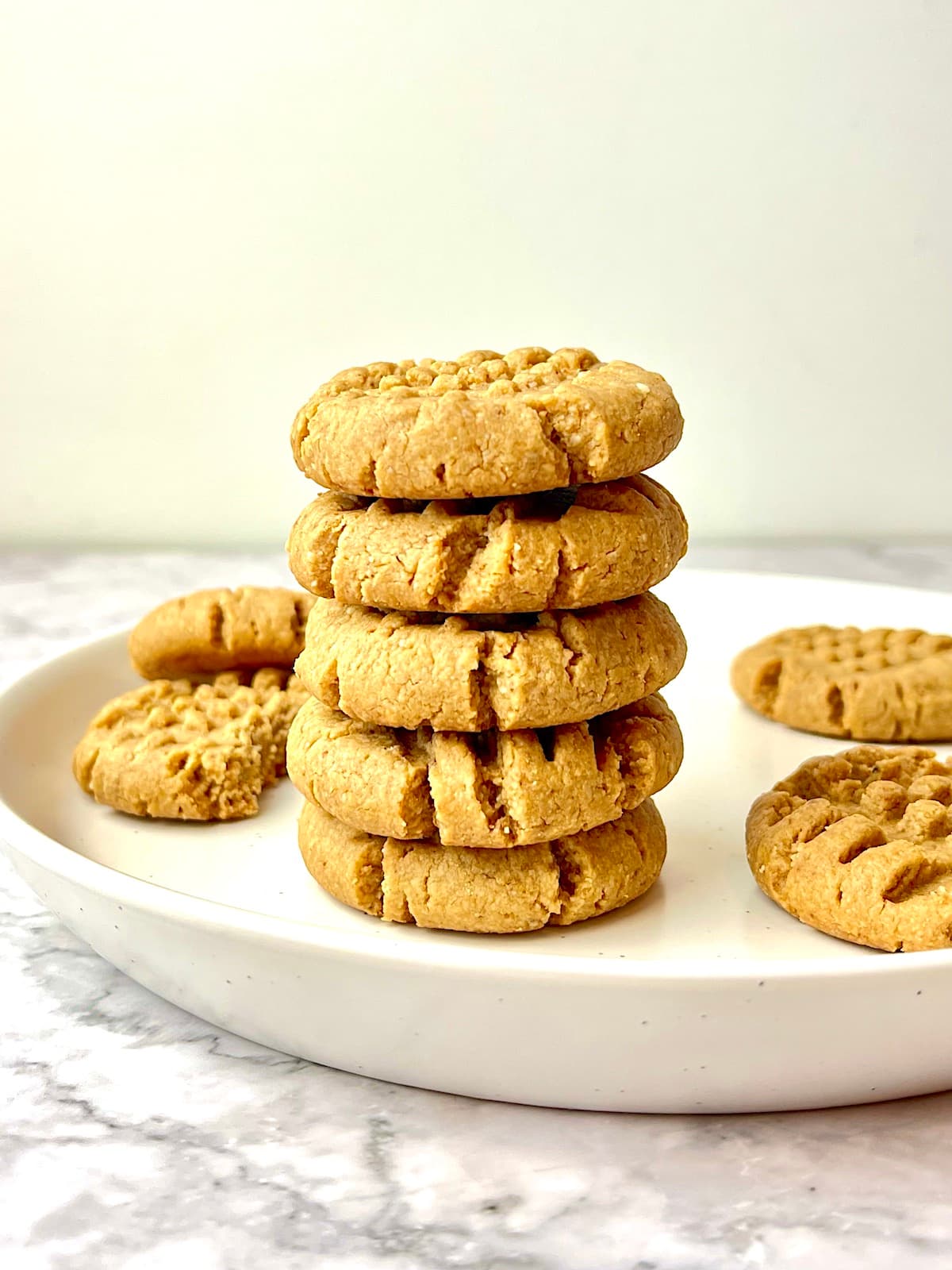 A stack of peanut butter cookies on a plate, surrounded by more peanut butter cookies.