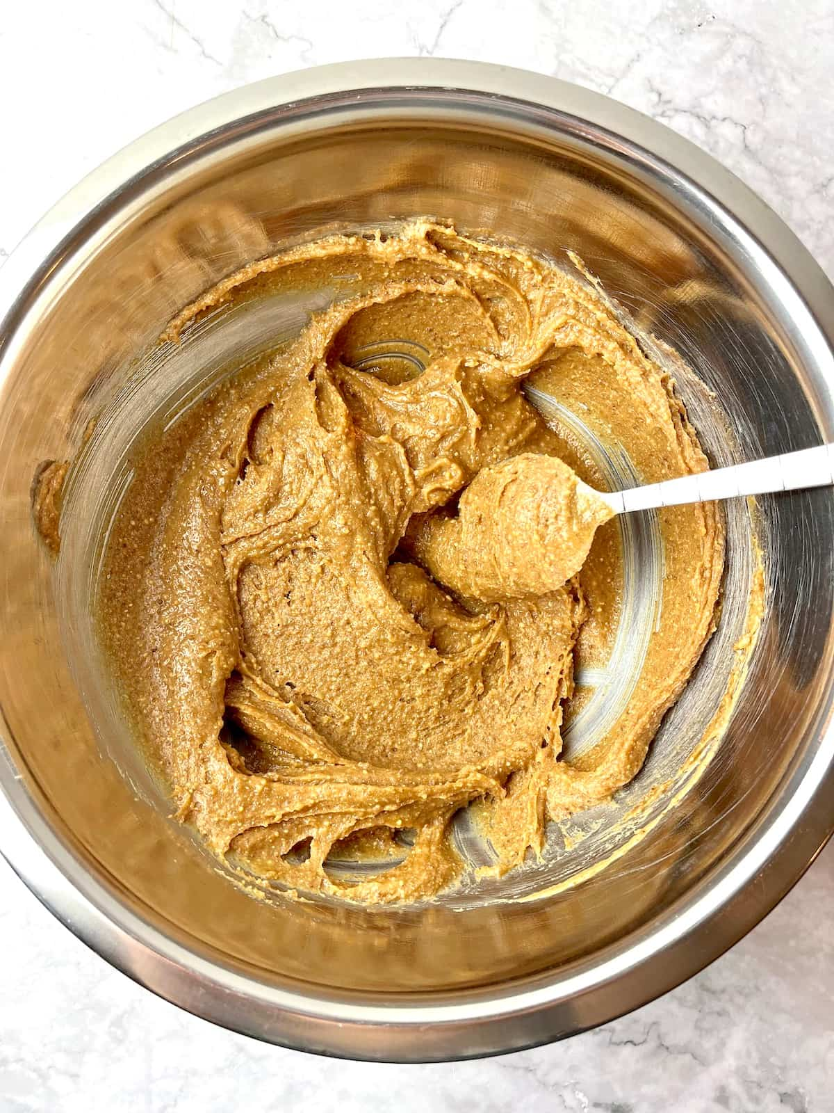 Peanut butter cookie ingredients mixed in a bowl with a spoon.