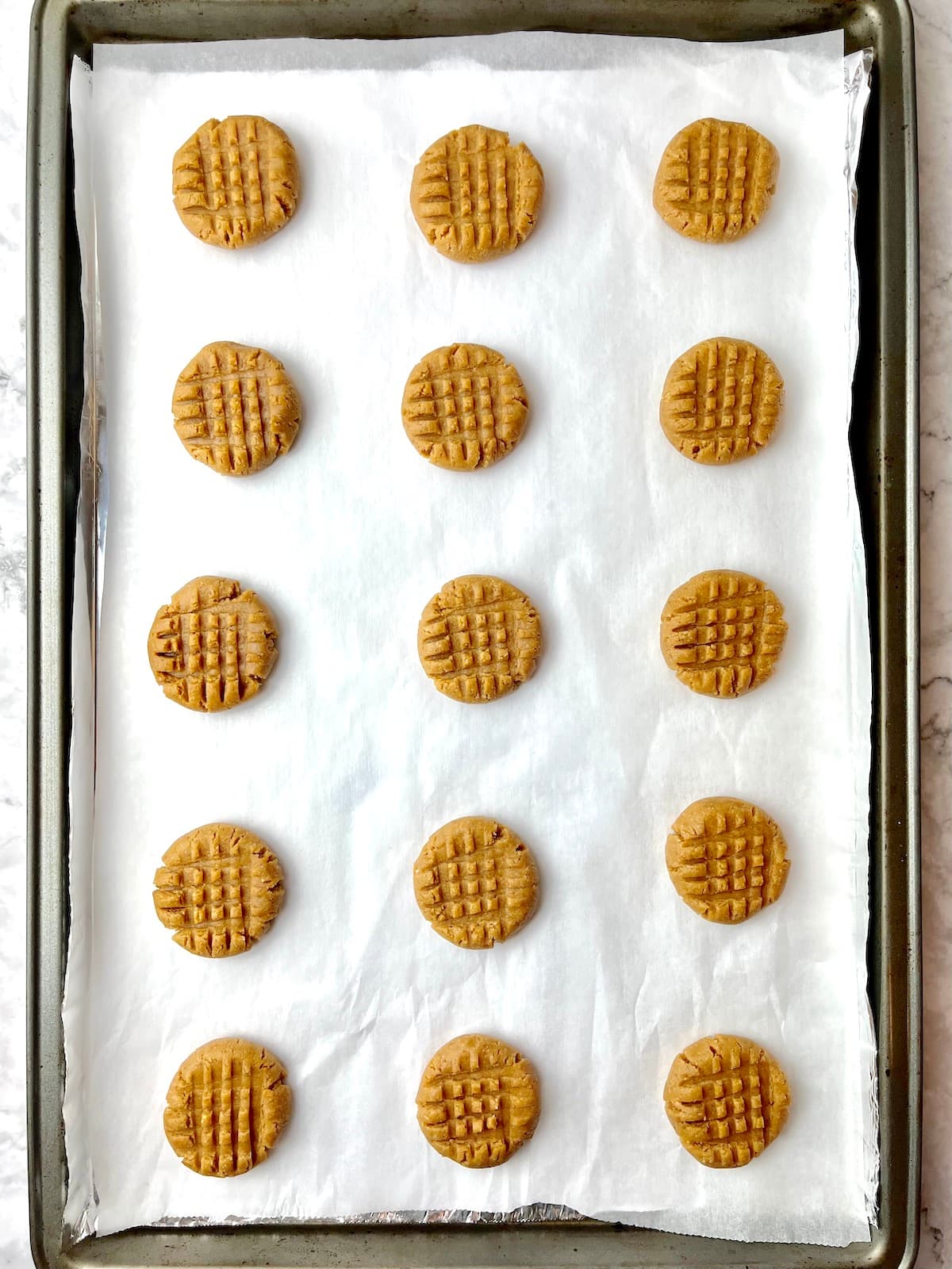 Peanut butter cookies before baking laid on a baking sheet.