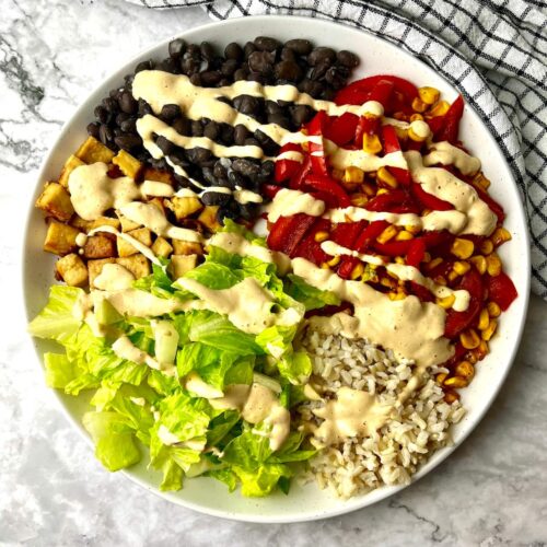 A vegan bowl with black beans, tofu, veggies, and rice, topped with a creamy vegan dressing.