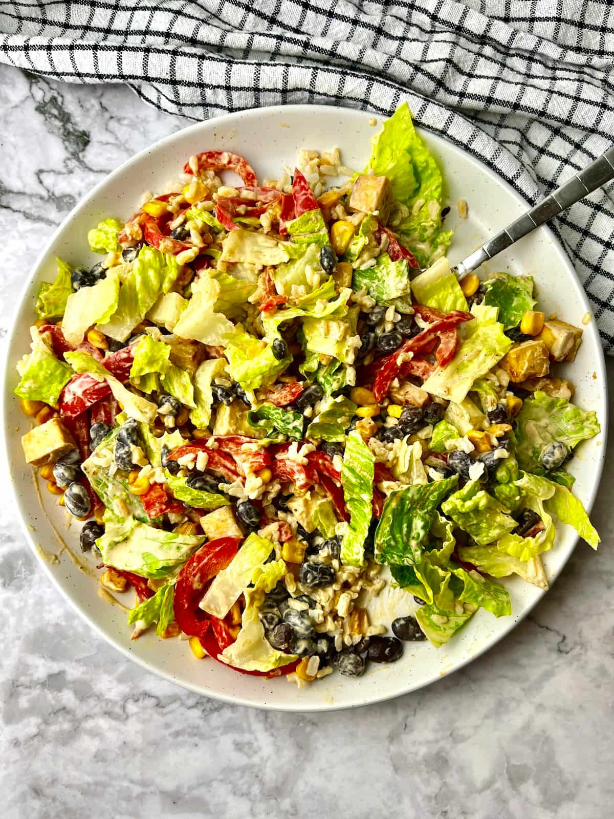 A vegan high protein bowl mixed together with lettuce, veggies, rice, tofu, and black beans.