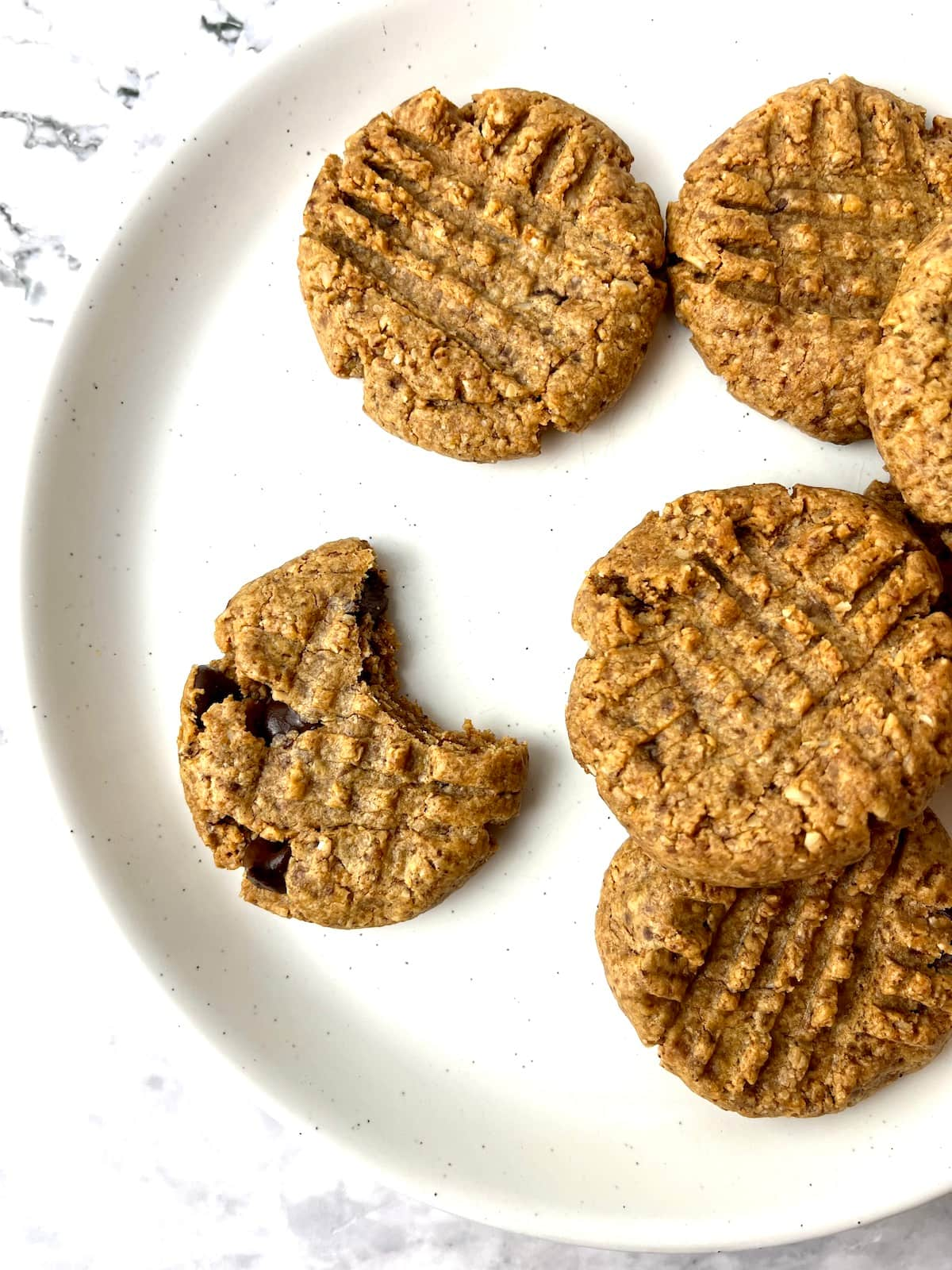 A plate of vegan almond butter cookies, one with a bite taken out.