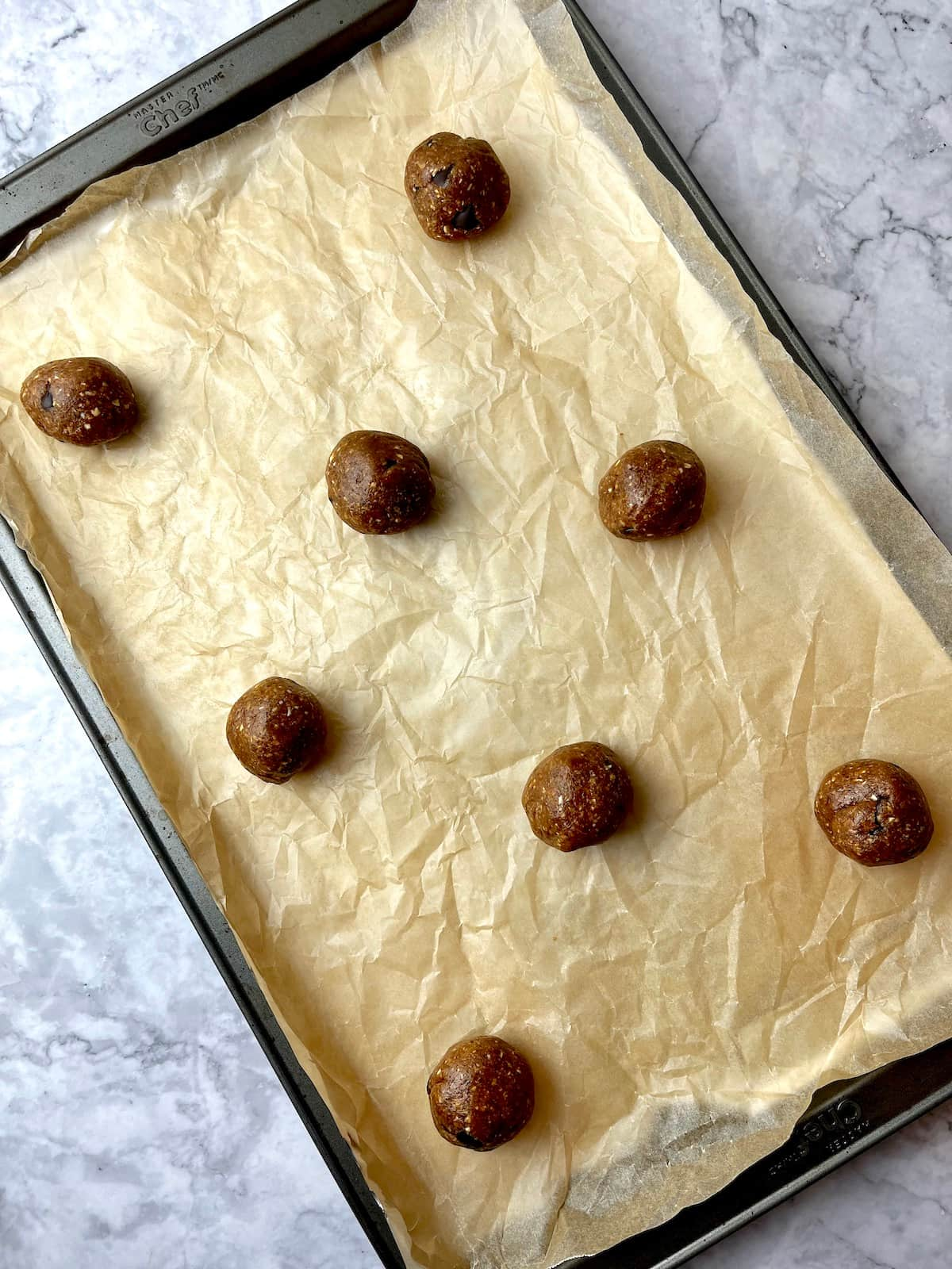 Vegan almond butter cookie dough balls on a baking sheet lined with parchment paper.