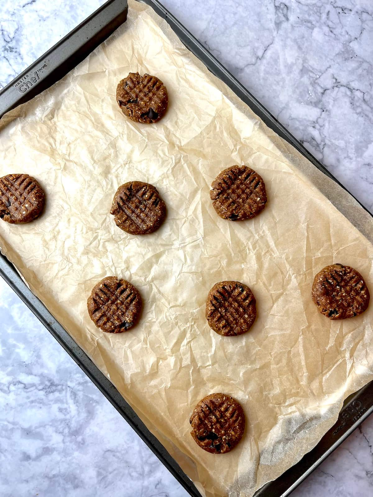 Vegan almond butter cookie dough pressed down on a baking sheet lined with parchment paper.