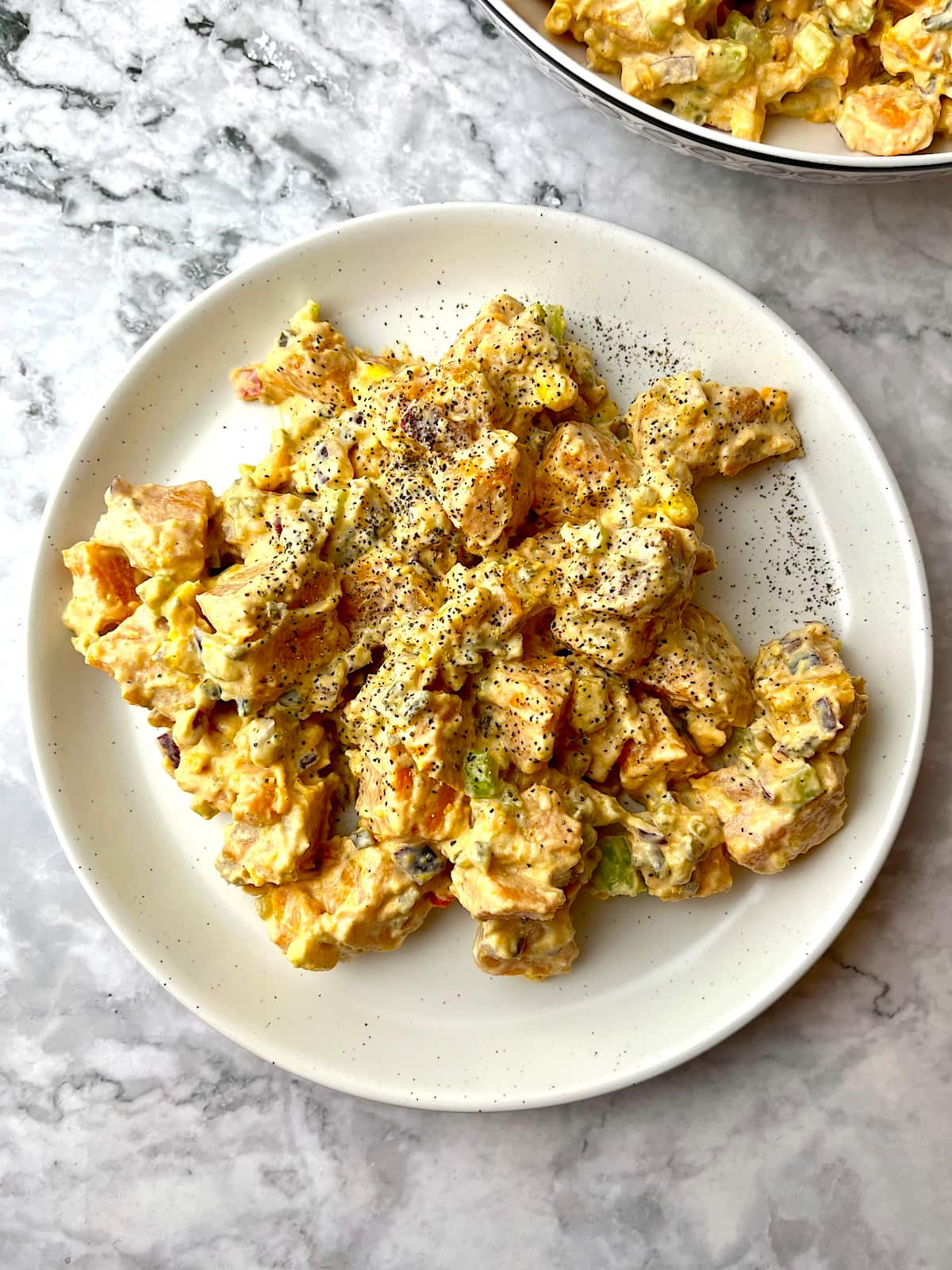 A plate of vegan sweet potato salad with ground black pepper sprinkled on top.