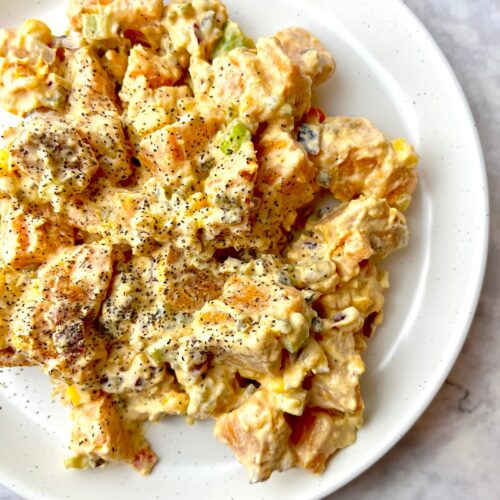 A plate of creamy vegan sweet potato salad with ground black pepper sprinkled on top.