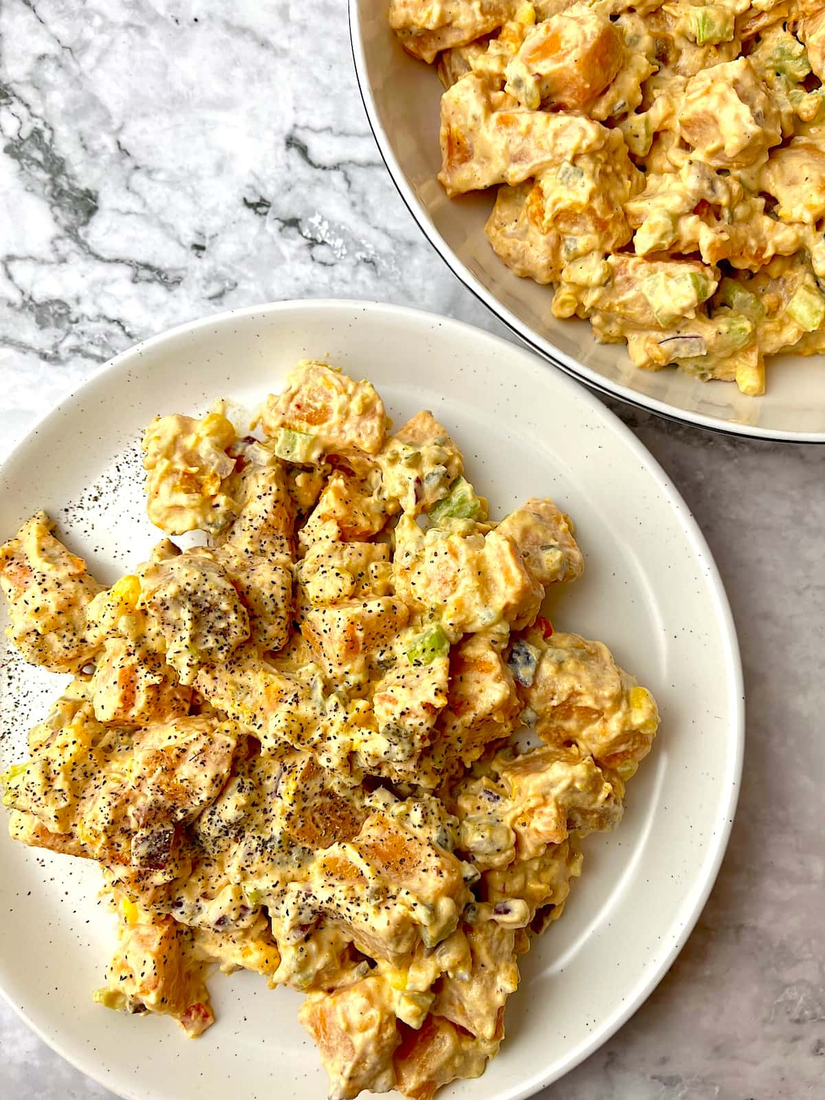 Two plates of sweet potato salad with a creamy vegan dressing and ground black pepper sprinkled on top.