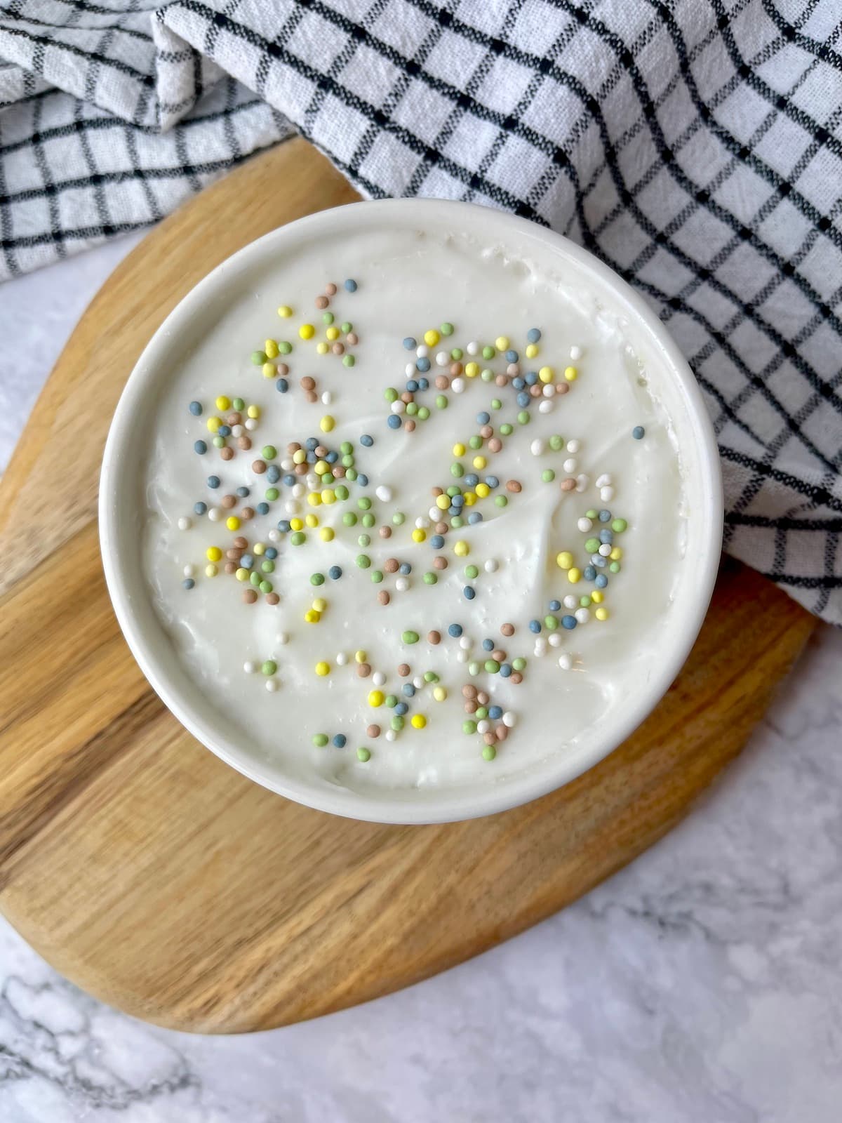 A vegan vanilla mug cake topped with white frosting and colorful sprinkles.