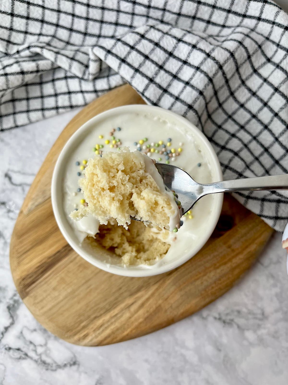 A spoonful of a vegan vanilla mug cake with frosting and sprinkles.