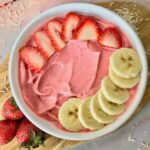 A strawberry banana smoothie bowl topped with slice banana and strawberry.