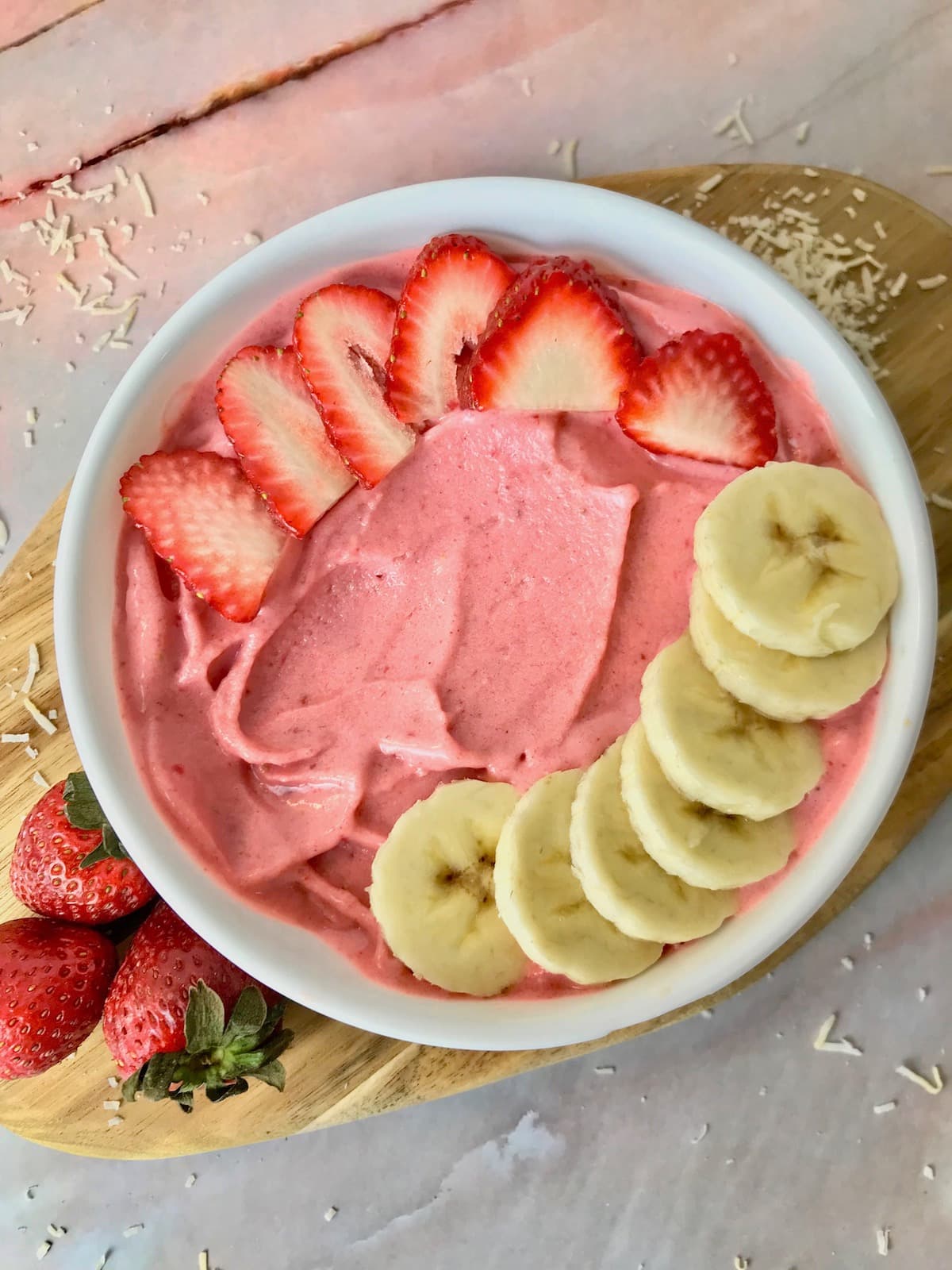 A strawberry banana smoothie bowl topped with slice banana and strawberry.