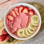 A strawberry banana smoothie bowl topped with slice banana and strawberry.