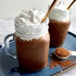 Two banana chocolate milkshakes topped with whipped cream with golden straws in them.