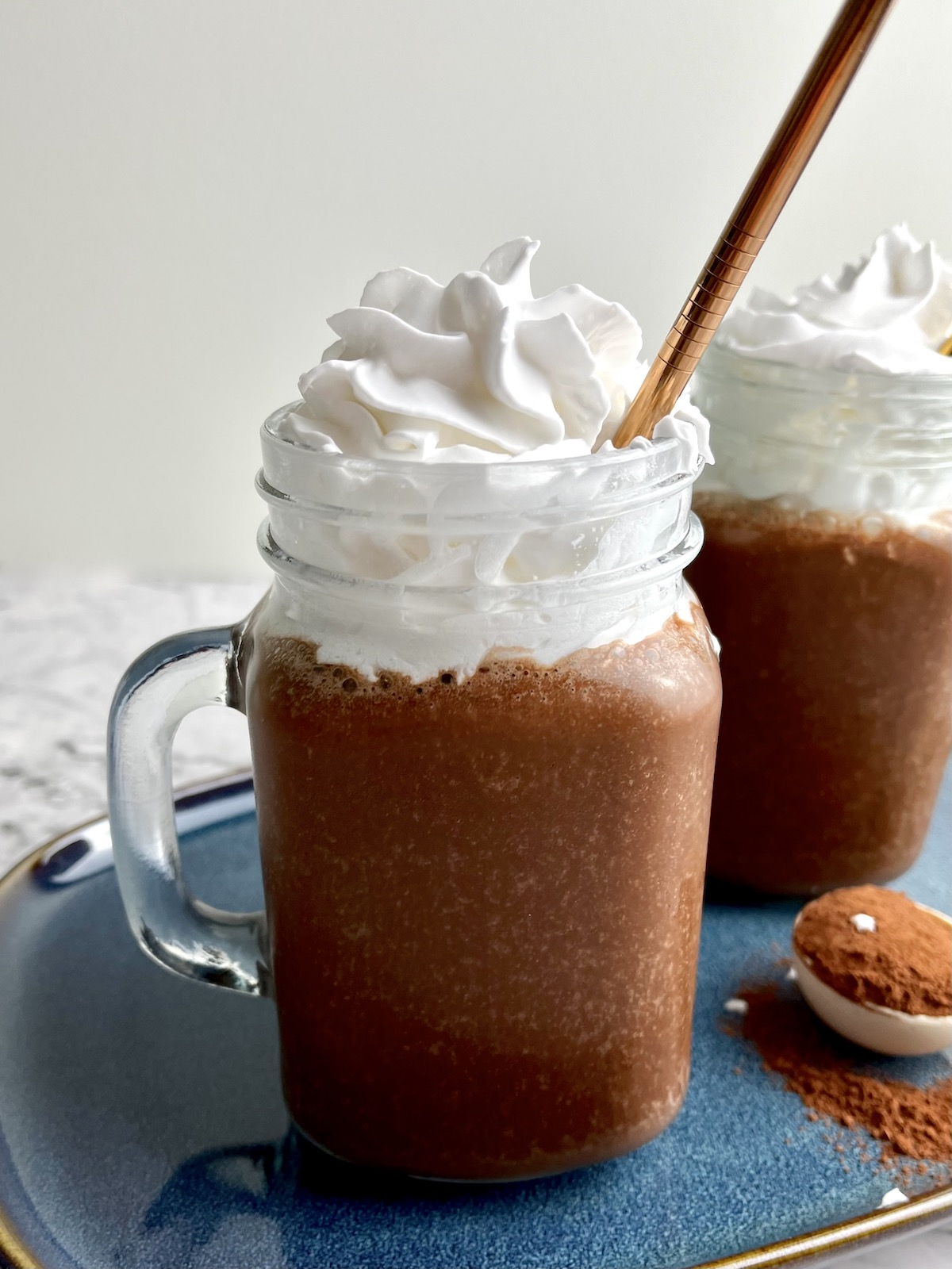 A banana chocolate milkshake topped with whipped cream with a golden straw in it.